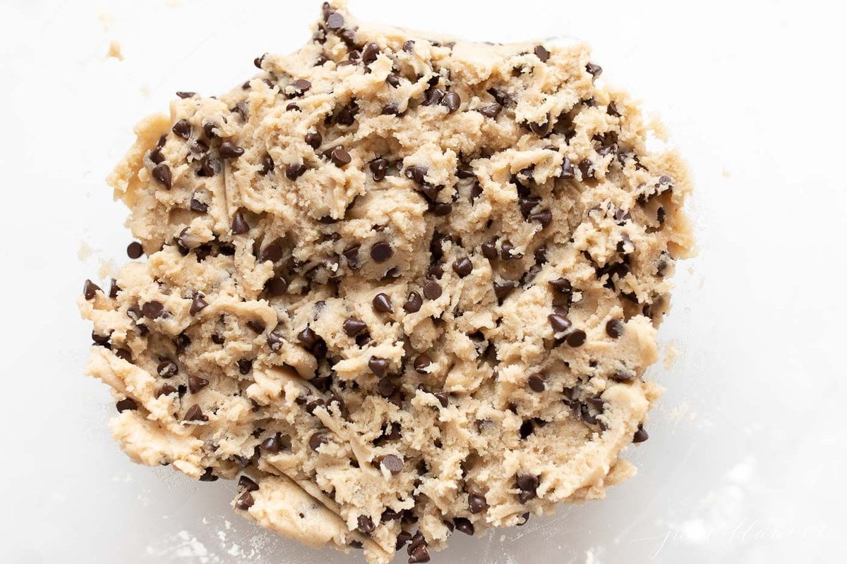 A small white bowl full of edible cookie dough with chocolate chips, on a marble surface