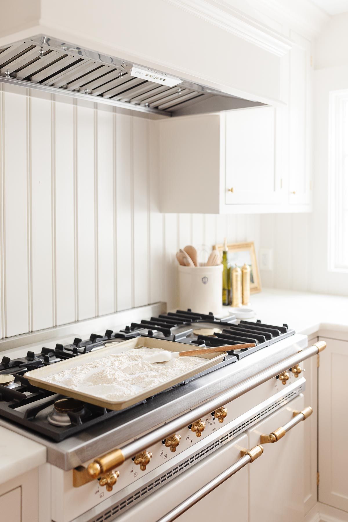 A baking sheet filled with all purpose flour, on top of an oven with brass knobs.