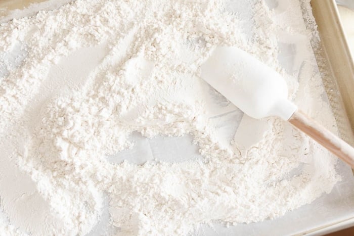 Flour on a baking sheet, being spread out with a white spatula