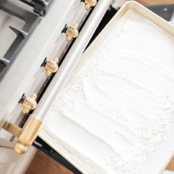 A baking sheet with flour in a white oven, as part of a tutorial for how to heat treat flour.