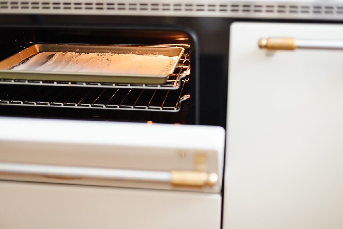 A baking sheet with flour in a white oven, as part of a tutorial for how to heat treat flour.