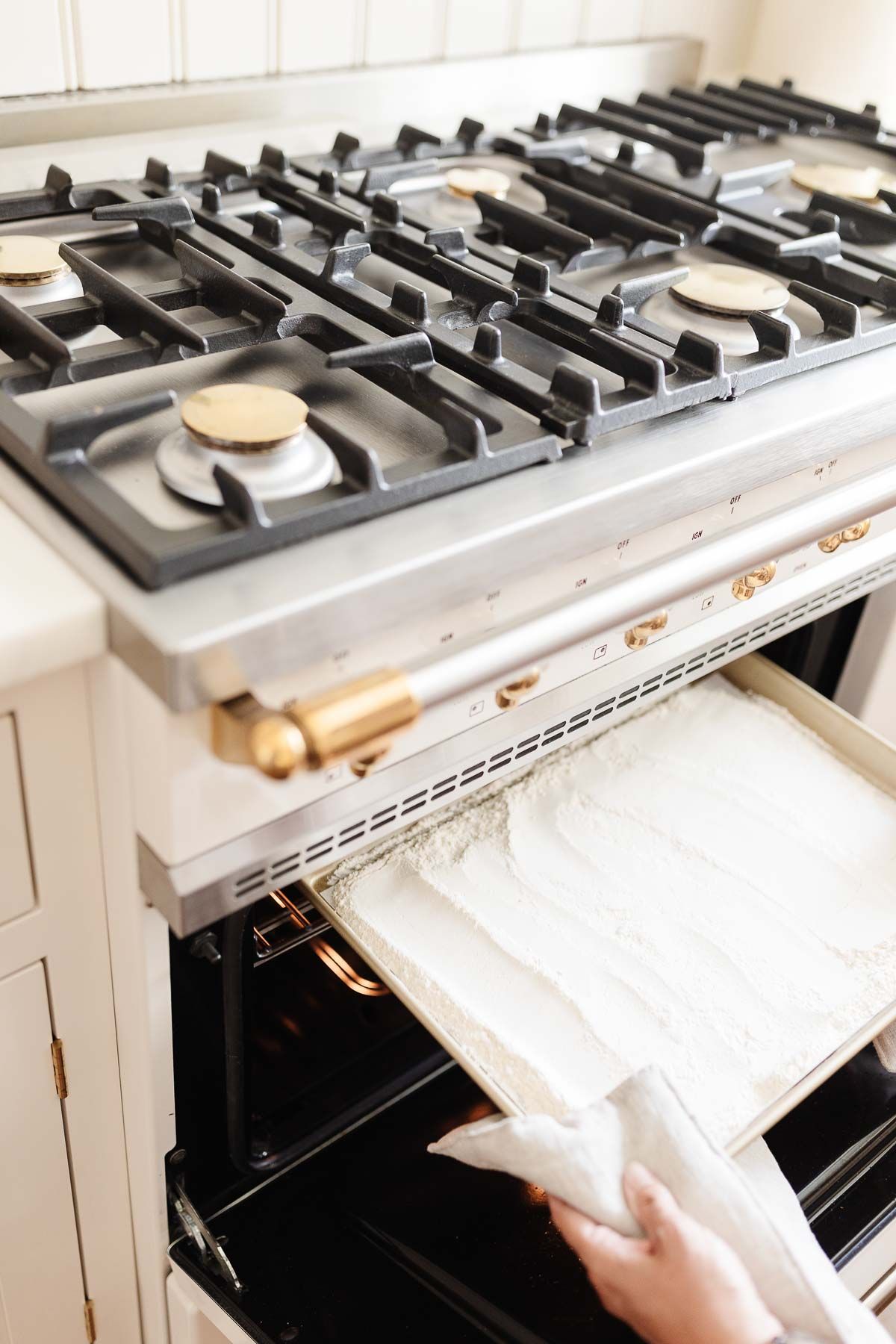 A baking sheet with flour in a white oven, as part of a tutorial for how to heat treat flour.