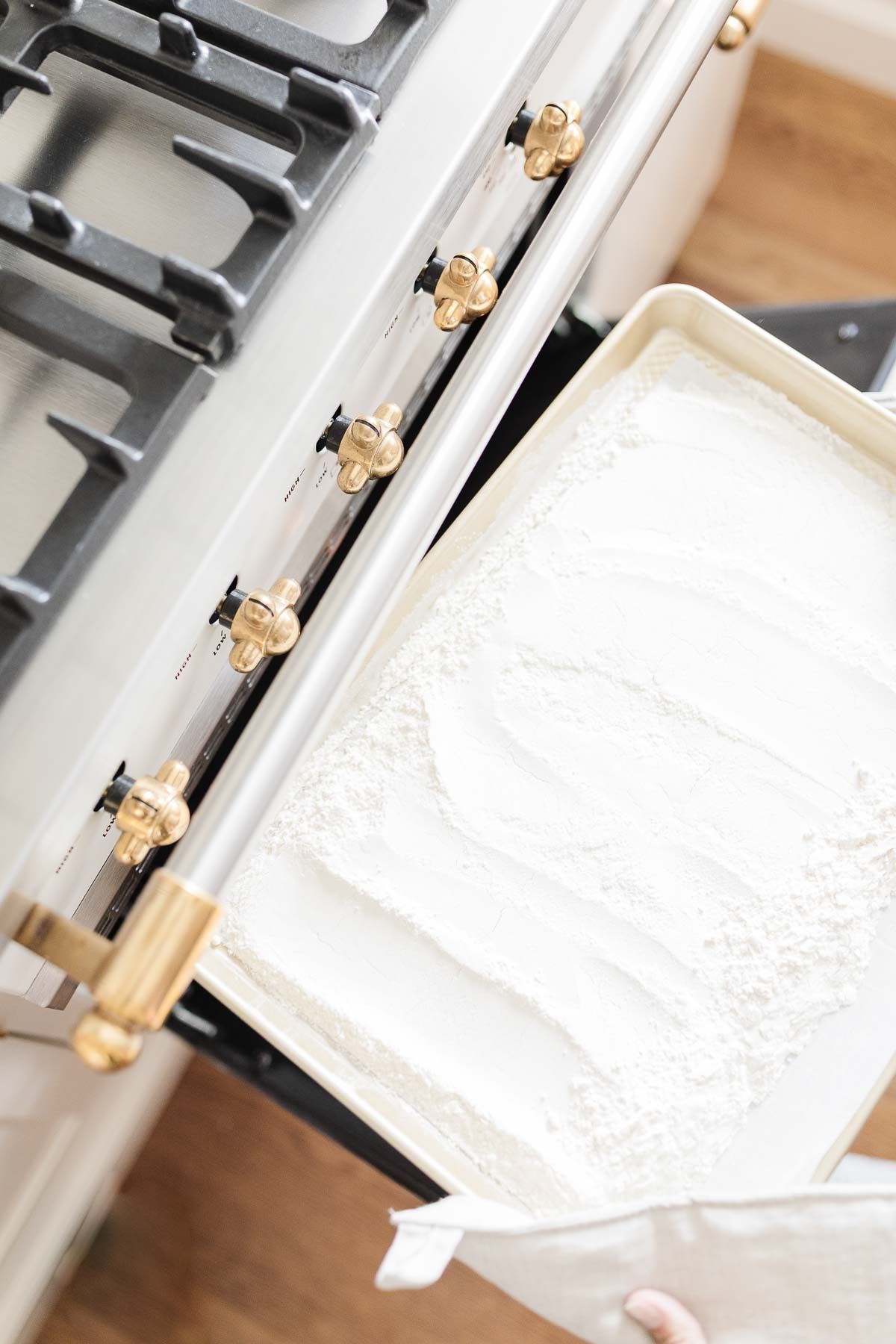 A baking sheet with flour in a white oven, as part of a tutorial for how to heat treat flour.