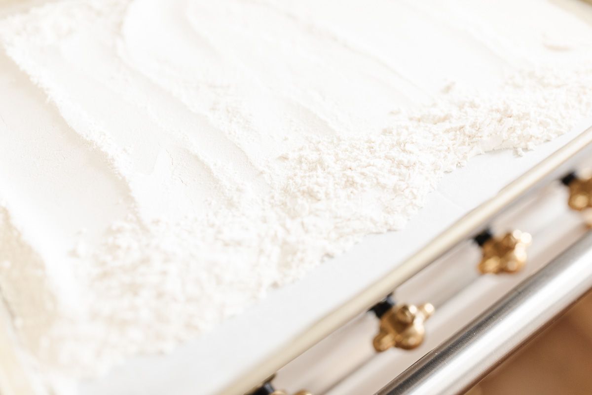 A baking sheet filled with all purpose flour, on top of an oven with brass knobs.