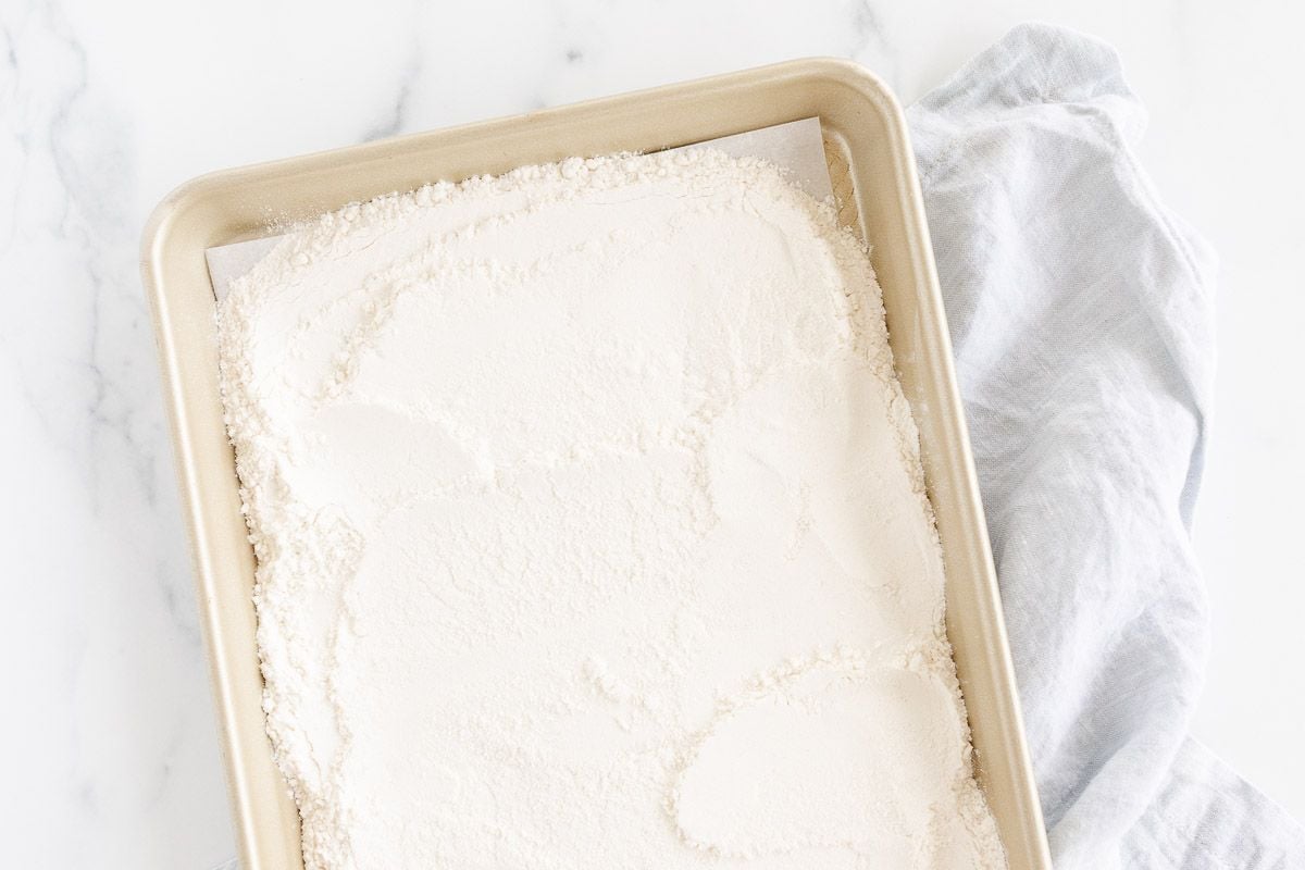 Flour spread out on a gold rimmed baking sheet, on a marble countertop