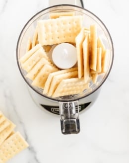 Club crackers in and around a small food processor, on a marble countertop.