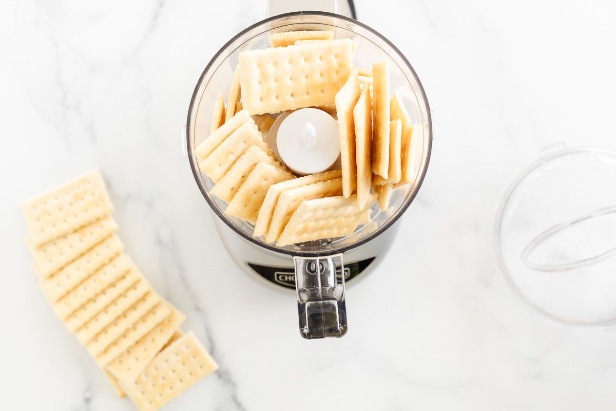 Club crackers in and around a small food processor, on a marble countertop.