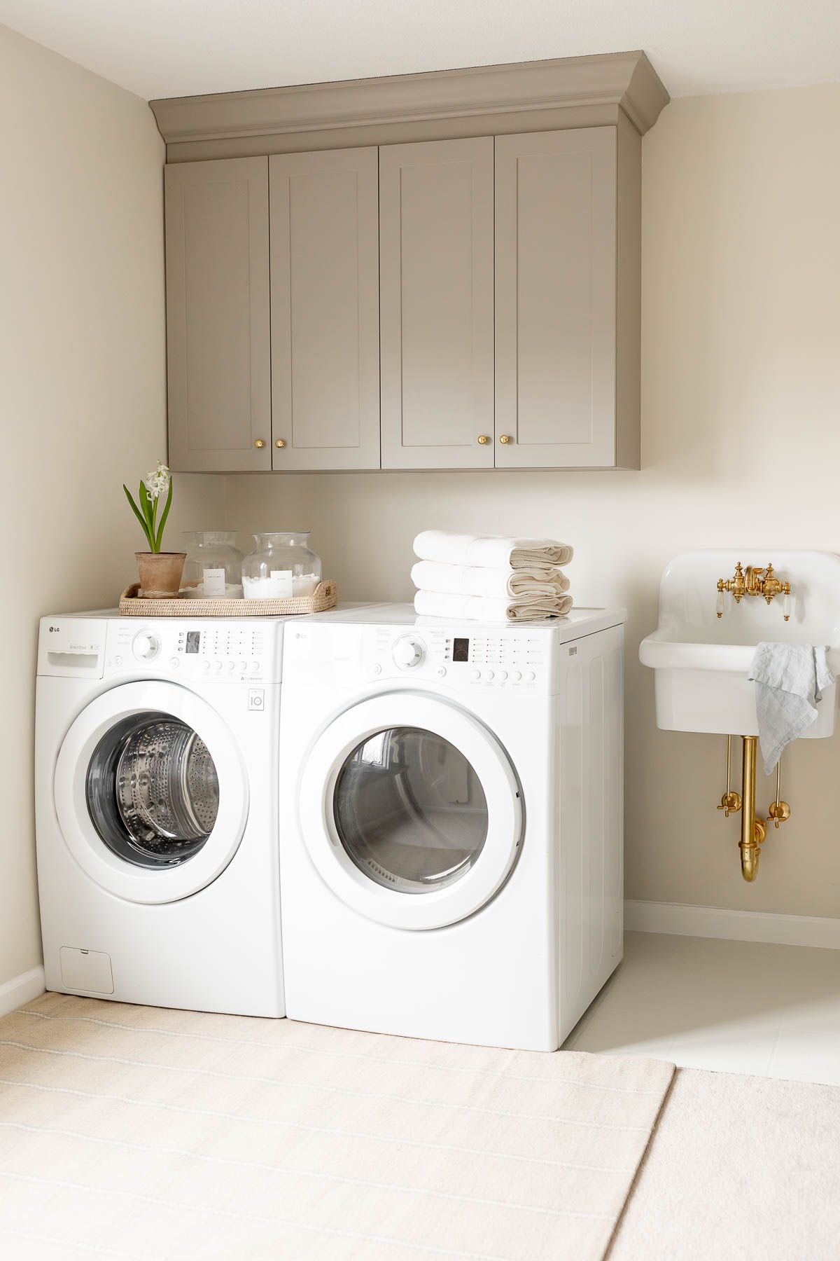 A laundry room with gray cabinets, white washer and dryer, and a plaid rug on carpet.