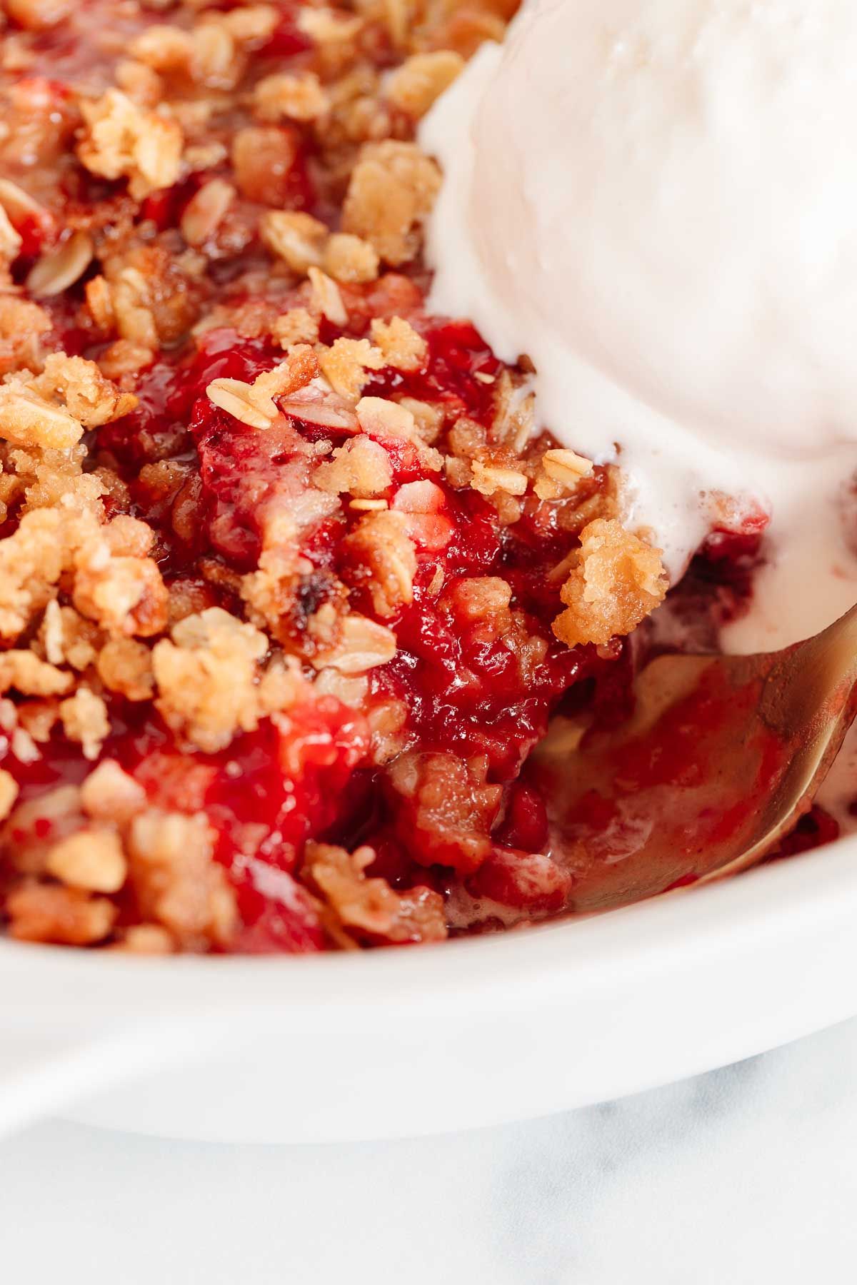 Close up of strawberry crumble topping after baking, topped with a scoop of vanilla ice cream
