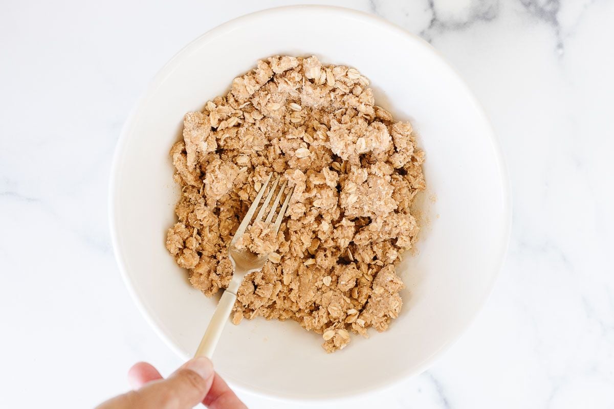 Crumble topping in a white bowl, being combined with a fork