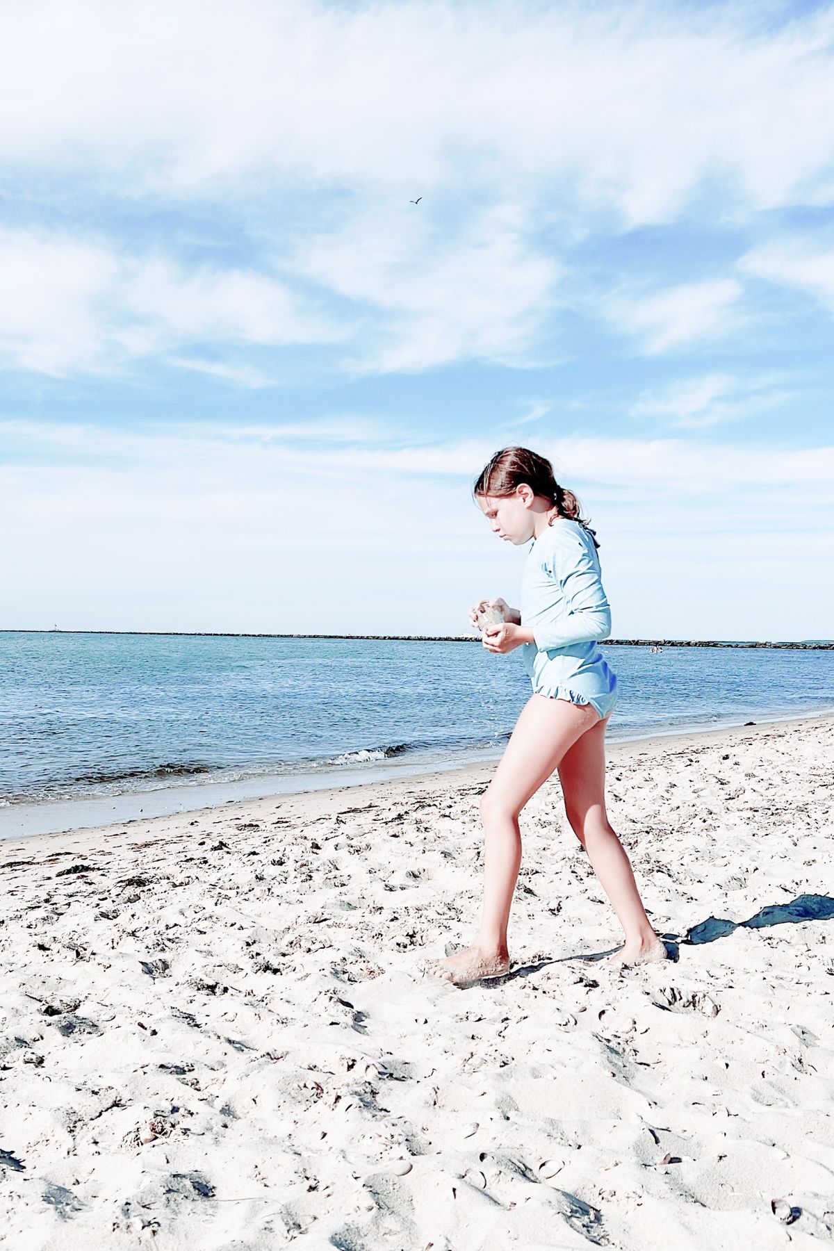 A little girl in a long sleeved blue bathing suit on a beach in Nantucket