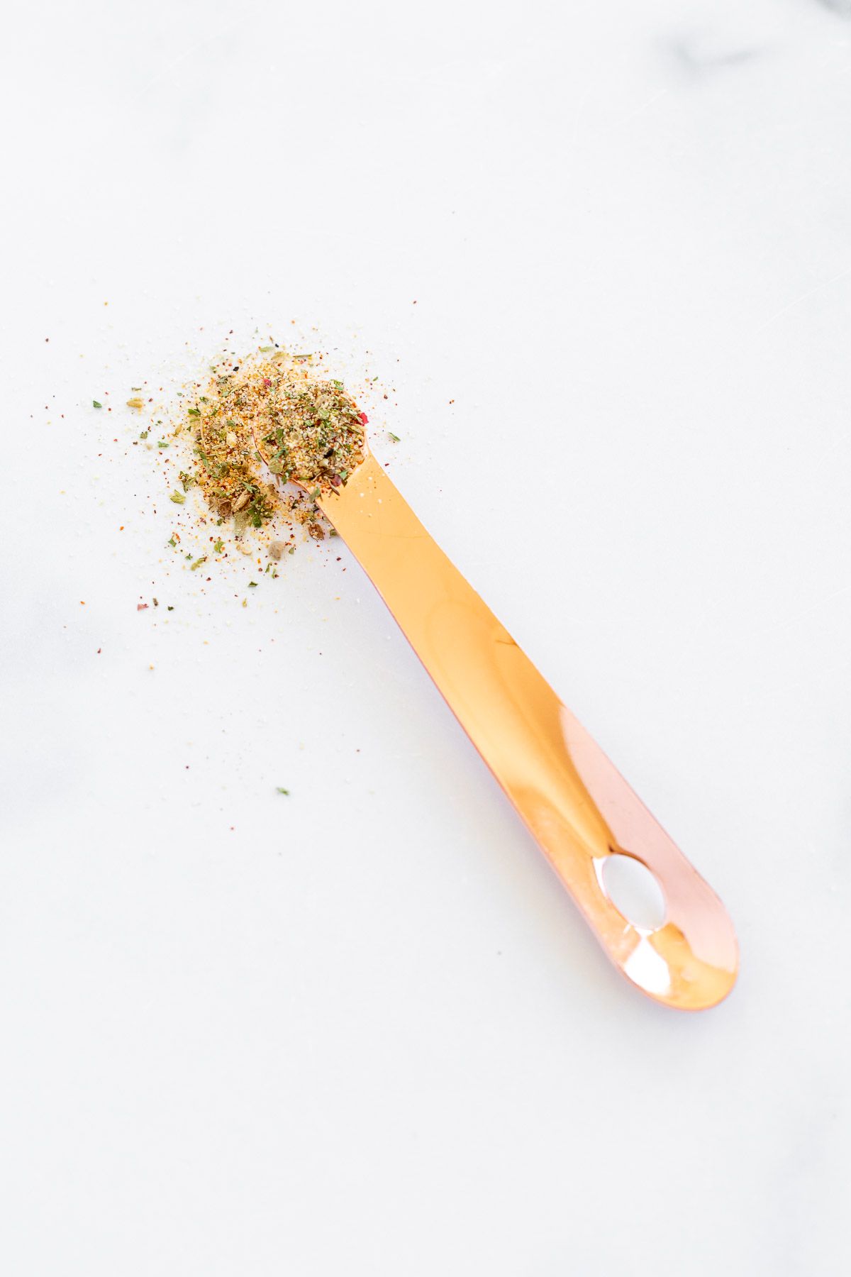 A copper teaspoon placed on a marble countertop, with all purpose seasoning.