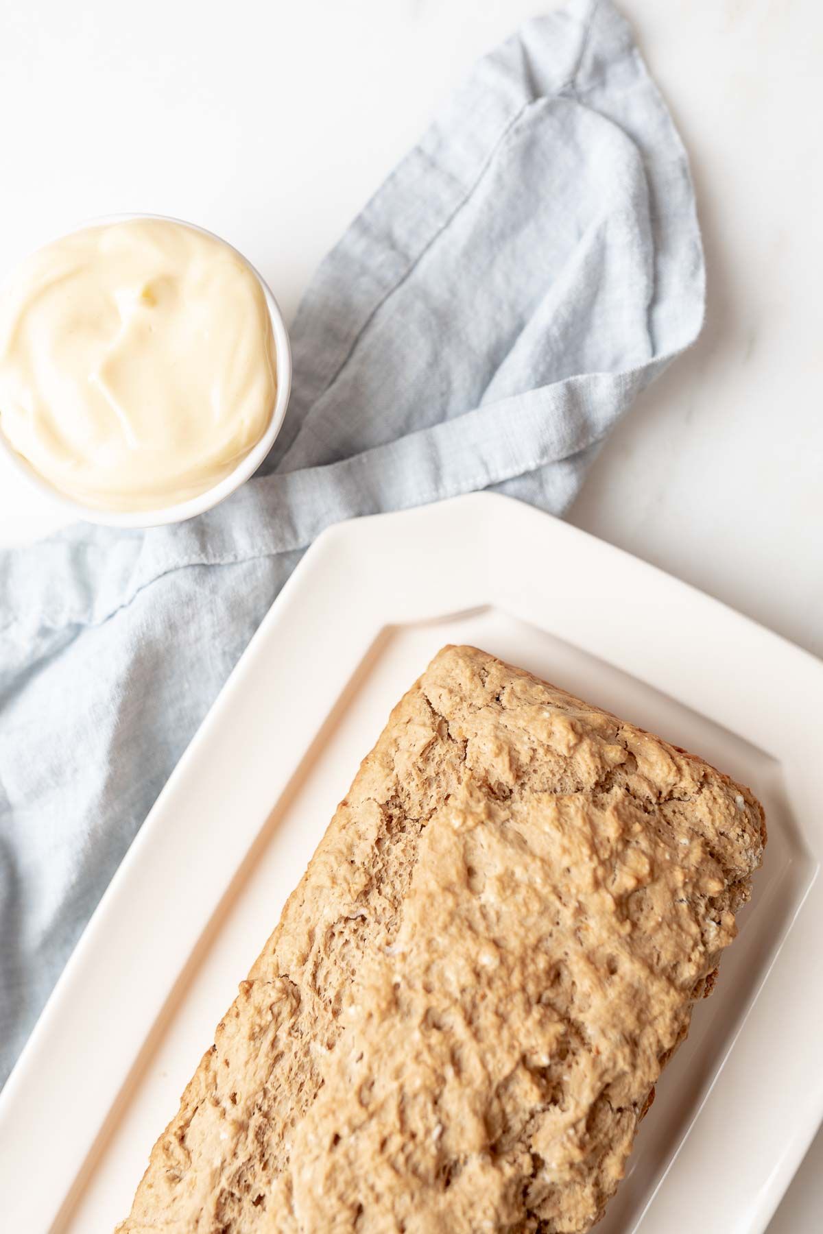 A loaf of beer bread on a white platter, with a small jar of honey butter to the side.