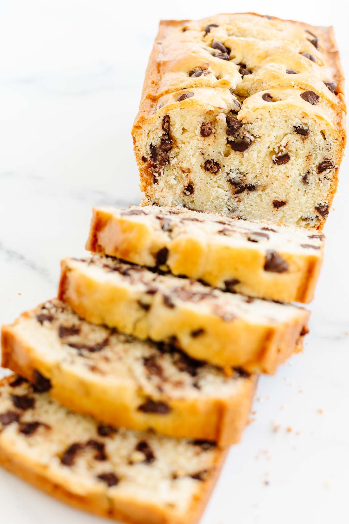 A chocolate chip bread loaf on a marble countertop, sliced for serving.