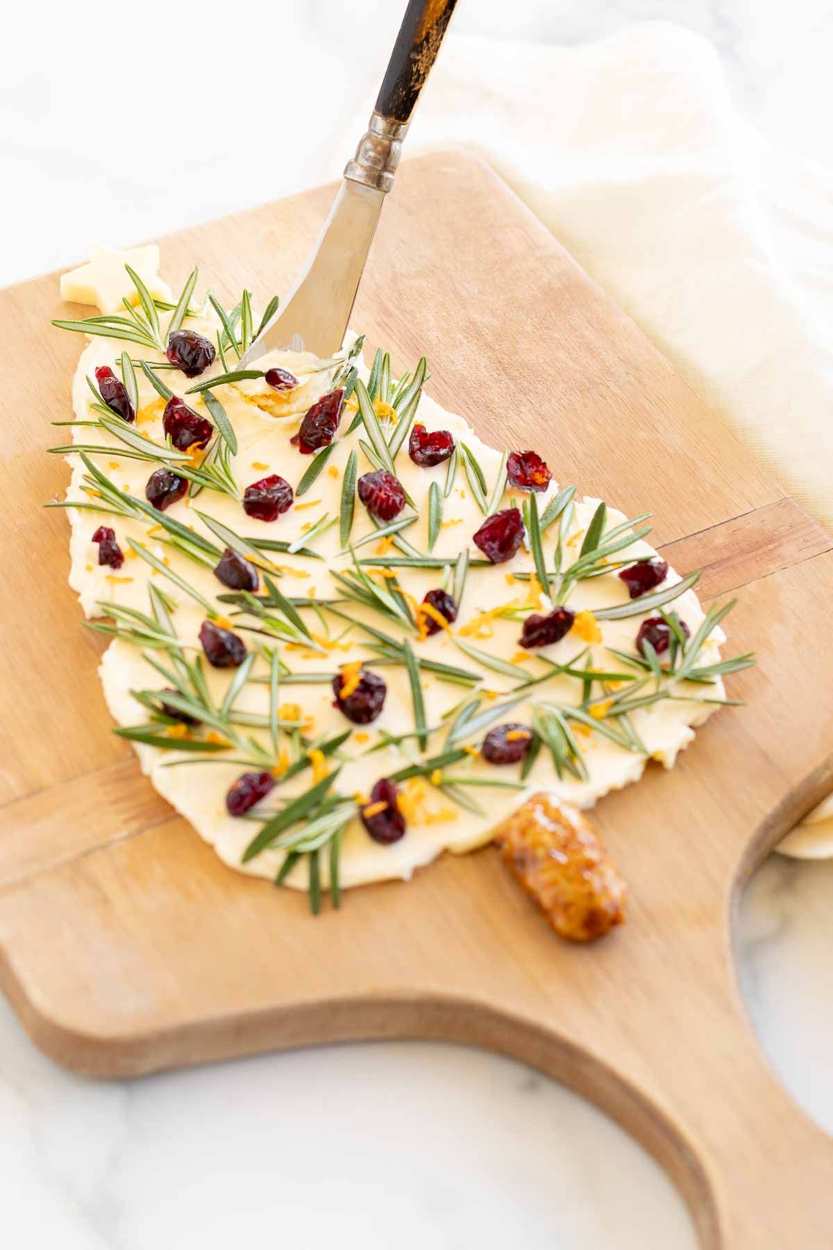 A Christmas butter board, placed on a wooden charcuterie board and shaped into a Christmas tree.