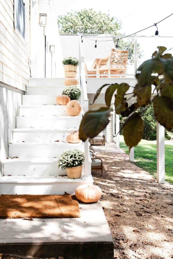 A white deck with steps that have fall decor ideas like white mums and pumpkins