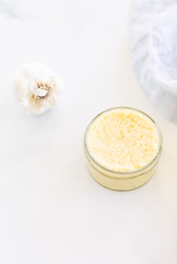 Garlic paste in a small clear glass jar, on a marble surface, garlic bulb in the background