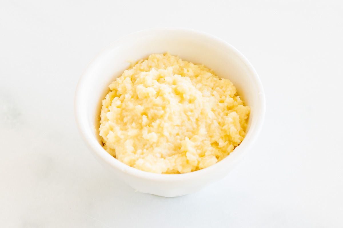 A white bowl of homemade garlic paste on a marble surface.