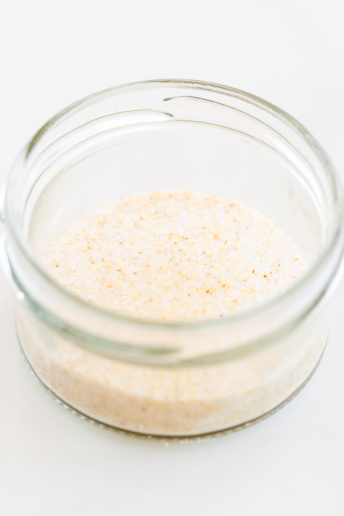 A small glass jar filled with homemade garlic salt, placed on a marble countertop.