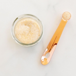 A small glass jar filled with homemade garlic salt, placed on a marble countertop. A copper measuring spoon is placed near the jar.