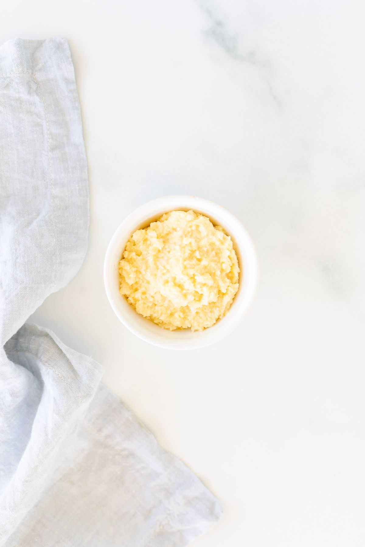 A white bowl of homemade garlic paste on a marble surface.