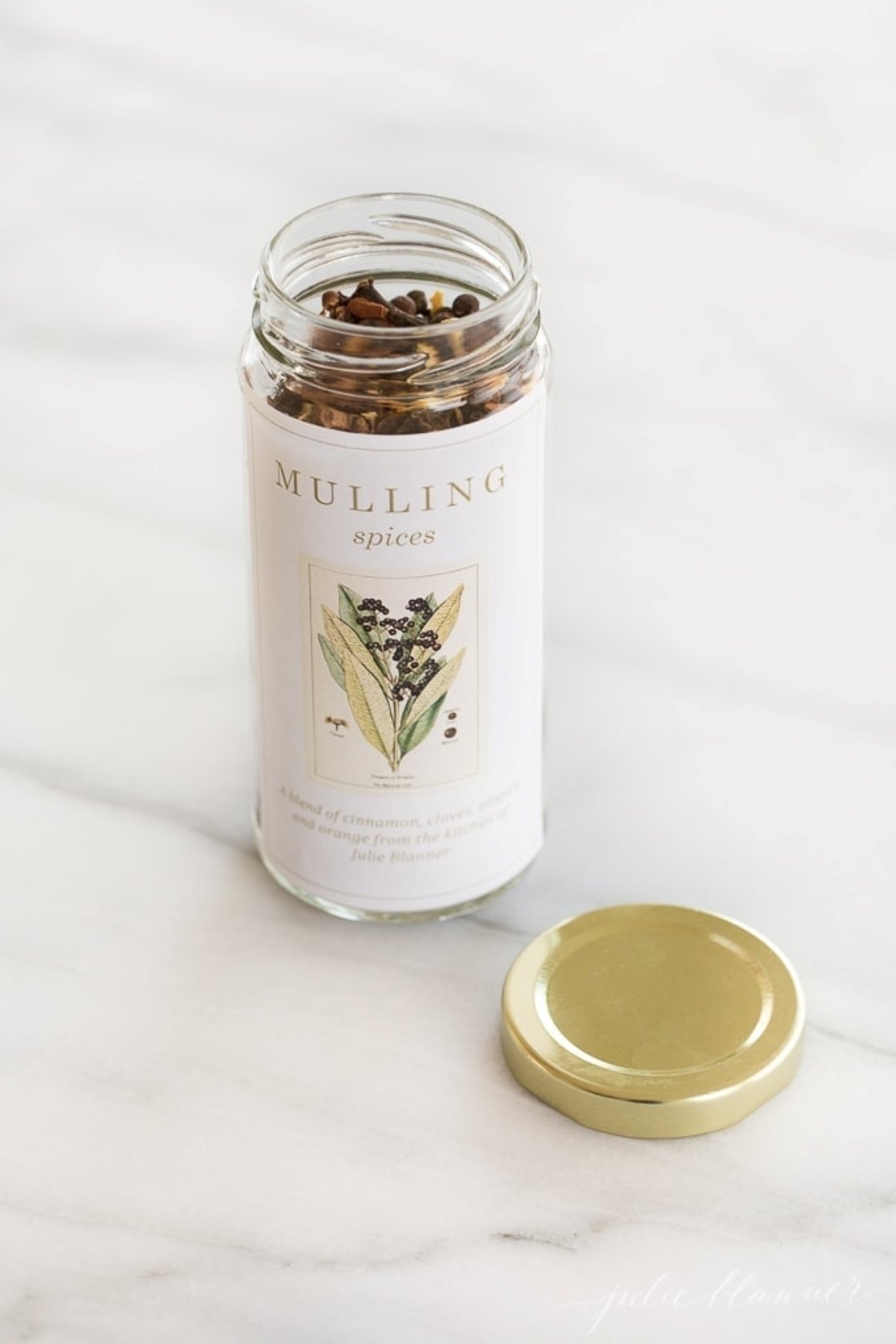 A bottle of mulling spices resting on a marble countertop, gold lid to the side.