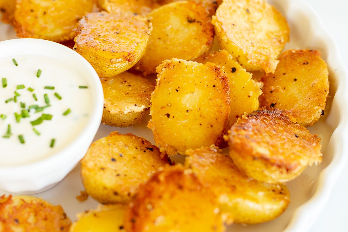 A white ruffled plate full of parmesan potatoes, with a small bowl of sour cream dip.