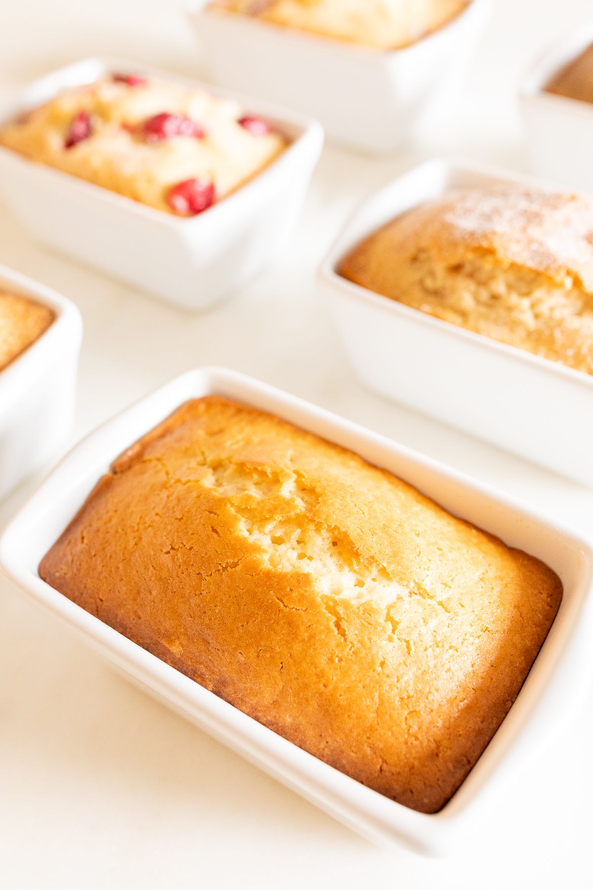 A variety of miniature loaves of quick bread recipes, baked into white ceramic loaf pans on a marble surface. 