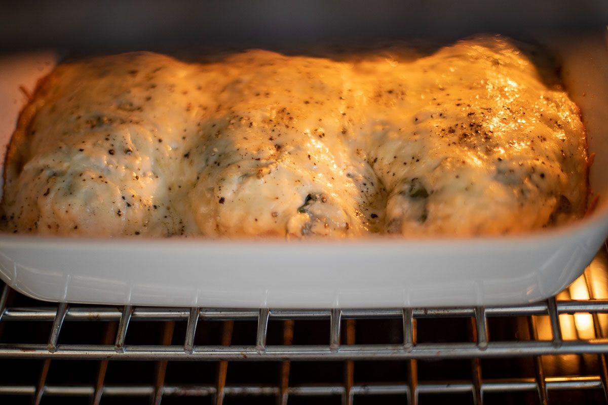 Baked chicken and spinach in a white casserole dish baking in an oven.