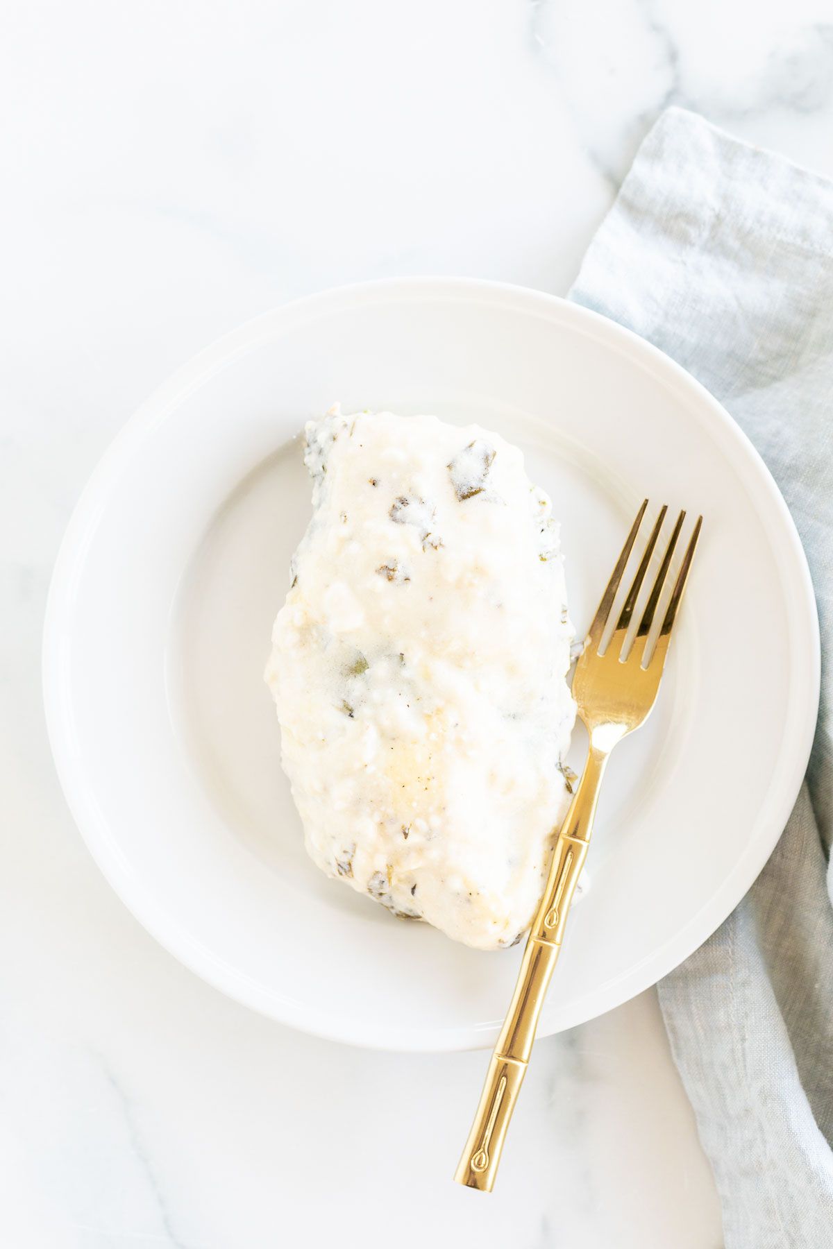 A baked chicken breast on a white plate, gold fork to the side.