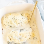 Baked chicken and spinach in a white casserole dish.
