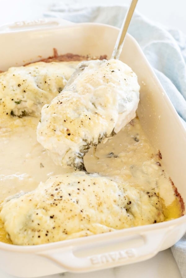 Baked chicken and spinach in a white casserole dish.