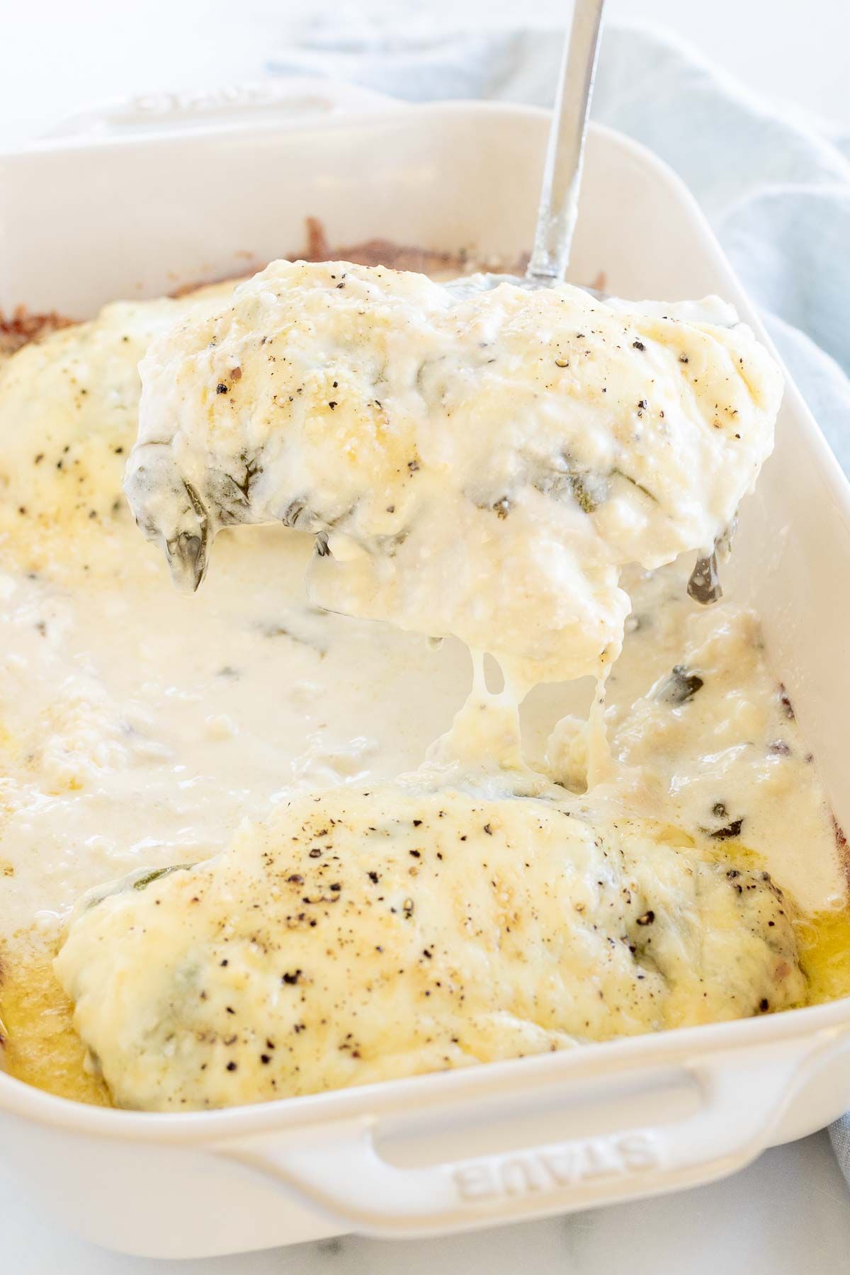 Baked chicken and spinach in a white casserole dish.