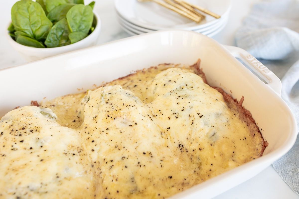 Baked chicken and spinach in a white casserole dish.
