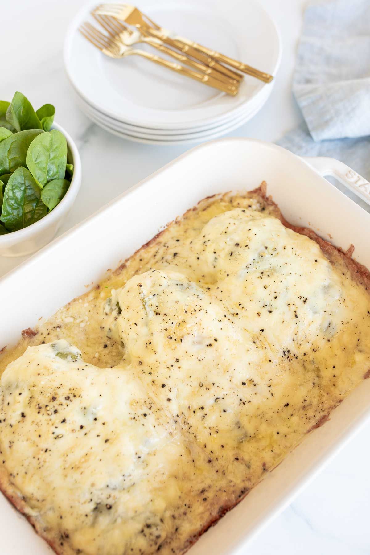 Baked chicken and spinach in a white casserole dish. 