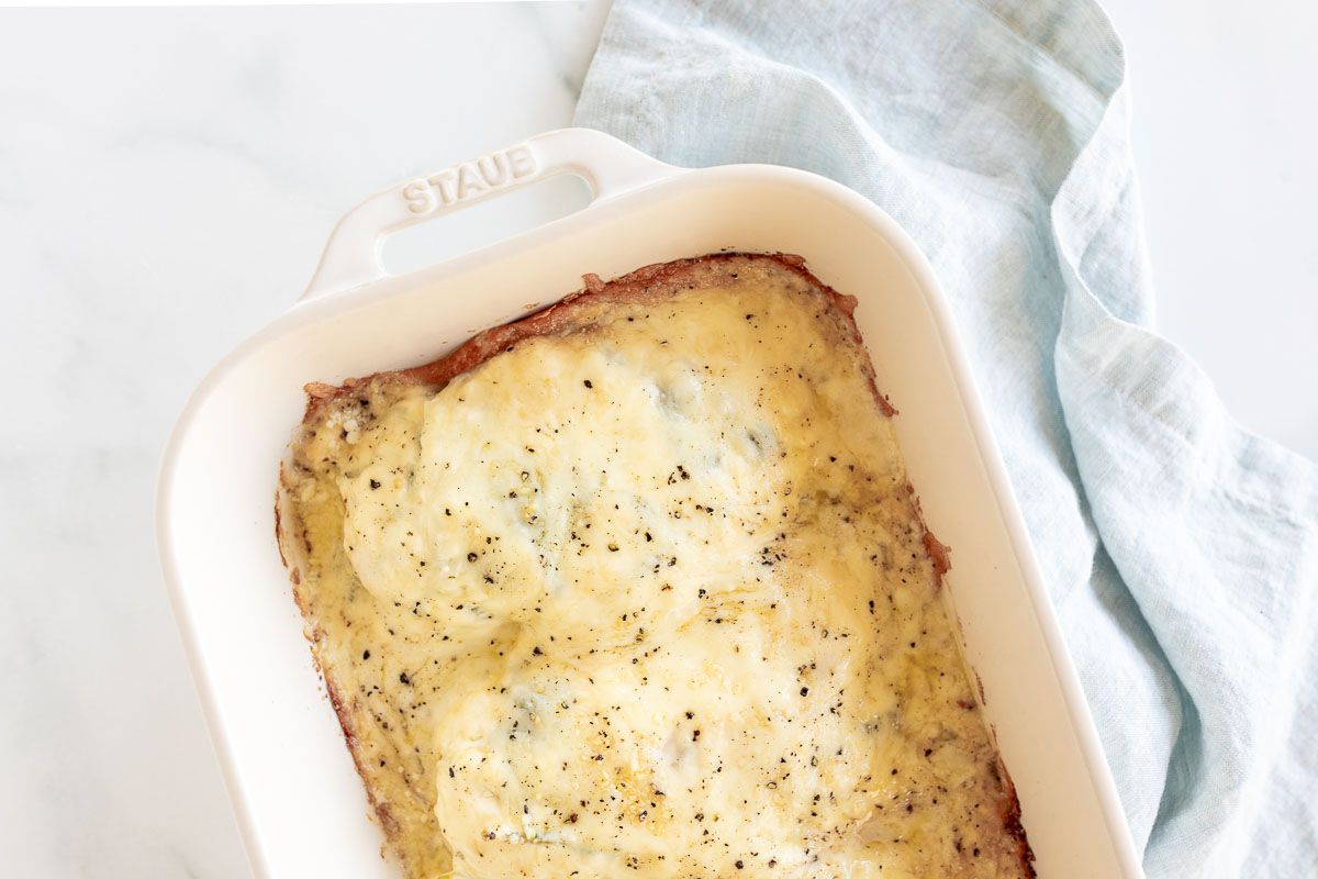 Baked chicken and spinach in a white casserole dish.