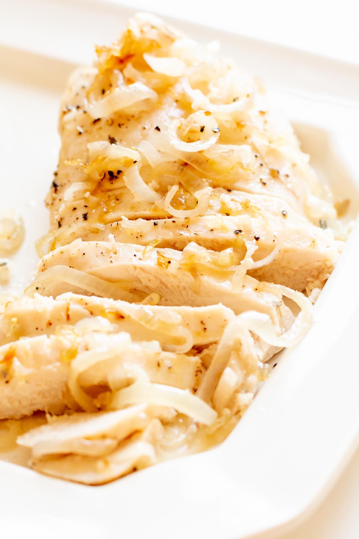 Sliced garlic chicken with shallots, on a white serving platter.