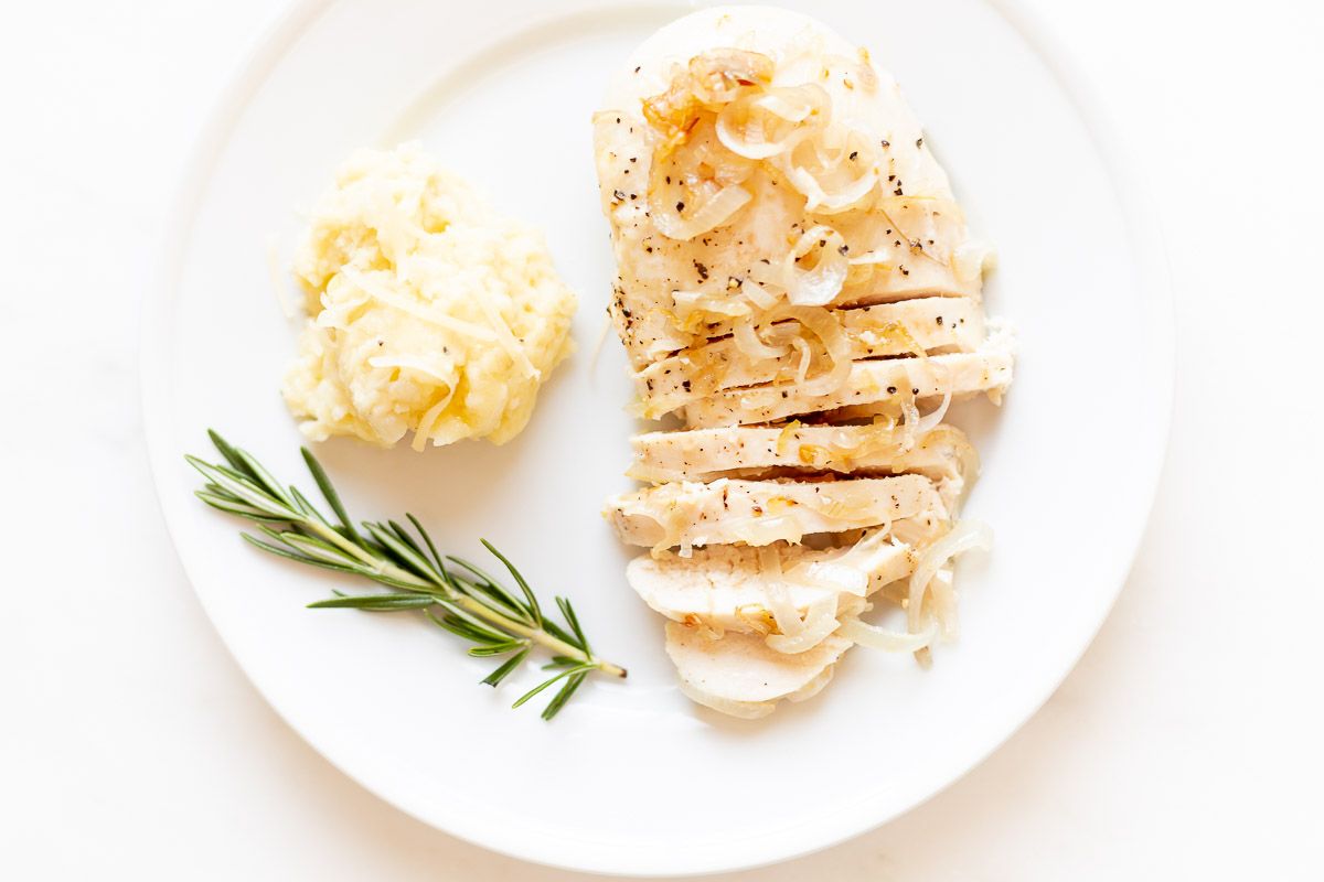 A white plate, topped with sliced garlic chicken with shallots, a scoop of mashed potatoes to the side.