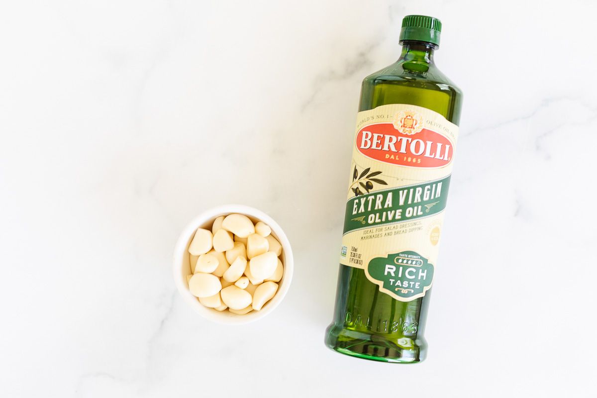 A small bowl of garlic cloves next to a bottle of olive oil for a tutorial on how to mince garlic