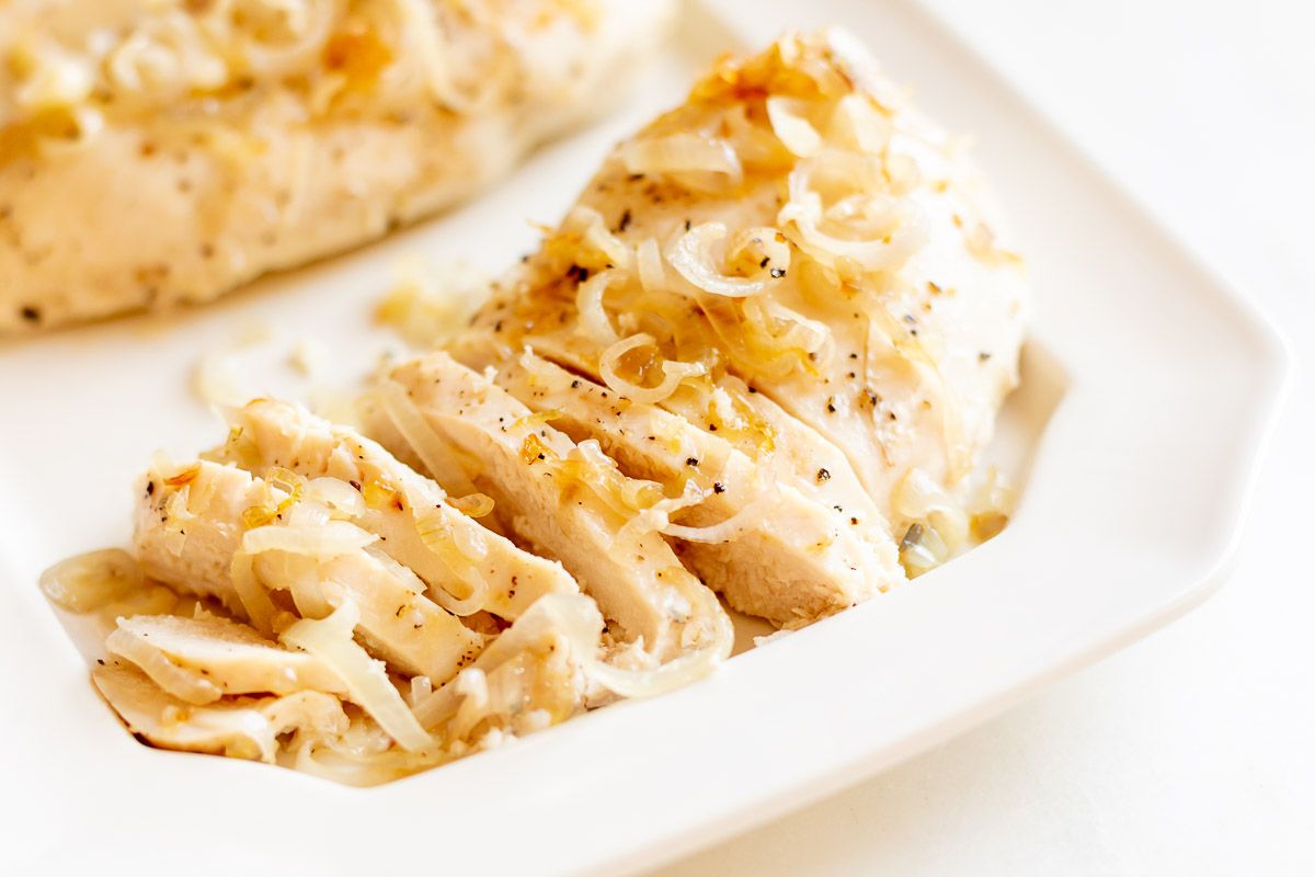 Sliced garlic chicken with shallots, on a white serving platter.