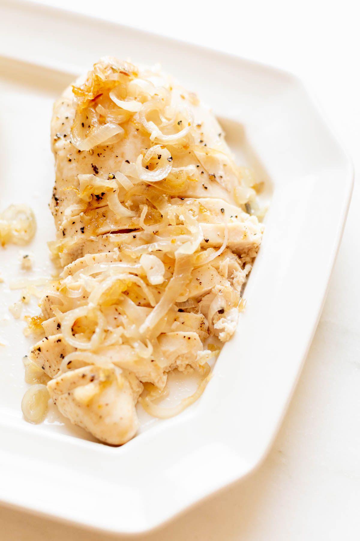 Sliced garlic chicken with shallots, on a white serving platter.