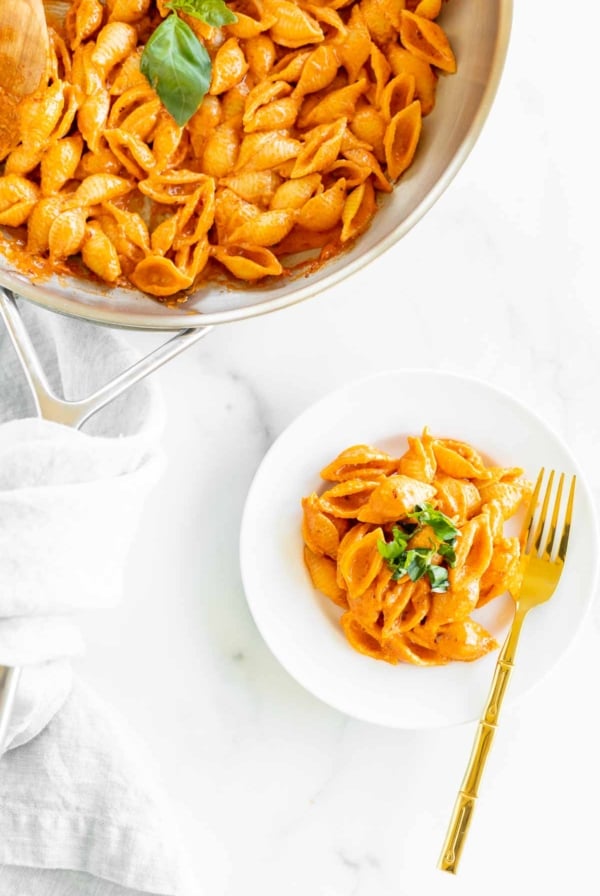 A white plate with a serving of Gigi Hadid pasta, a vodka pasta recipe. Gold fork on the side for serving, pan full of pasta on the side.