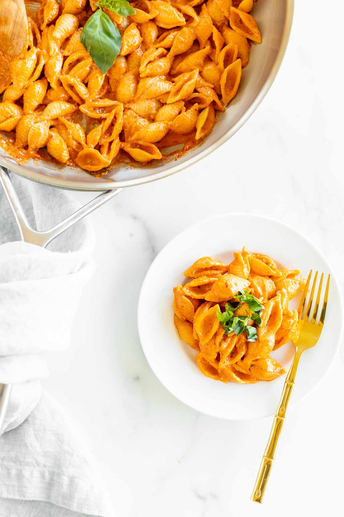 A white plate with a serving of Gigi Hadid pasta, a vodka pasta recipe. Gold fork on the side for serving, pan full of pasta on the side.