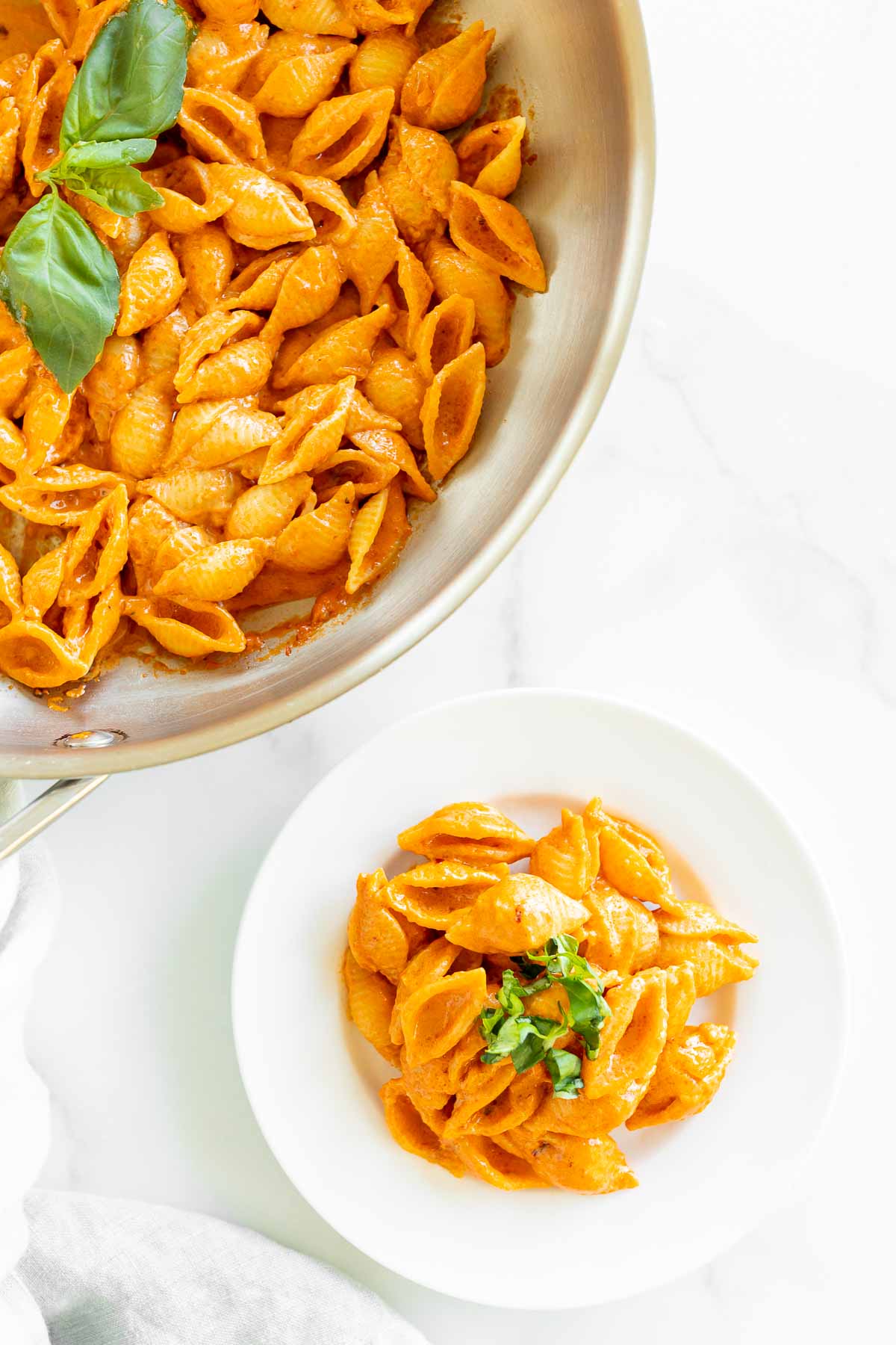 A white plate with a serving of Gigi Hadid pasta, a vodka pasta recipe. Gold fork on the side for serving, pan full of pasta on the side.