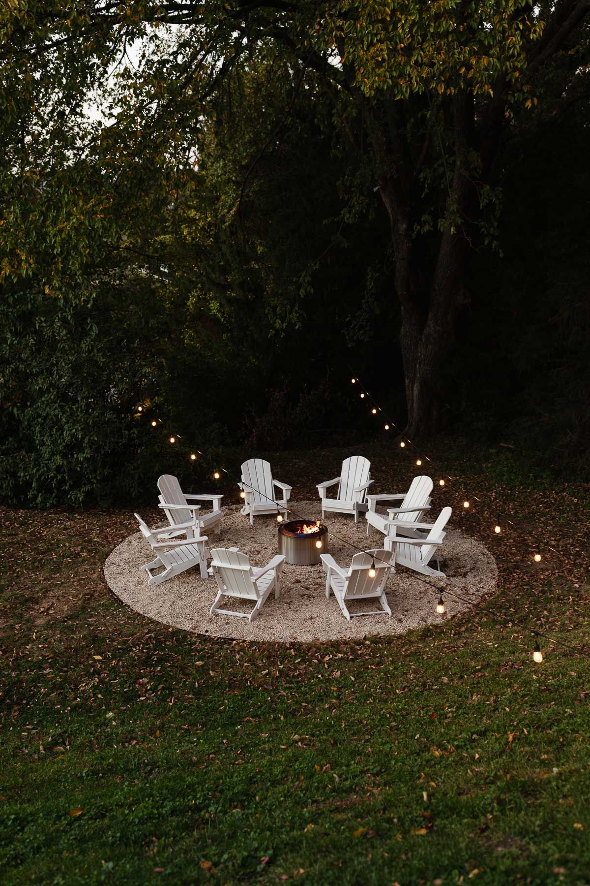 White Adirondack chairs, circling a Solo Stove on a DIY pea gravel fire pit patio.