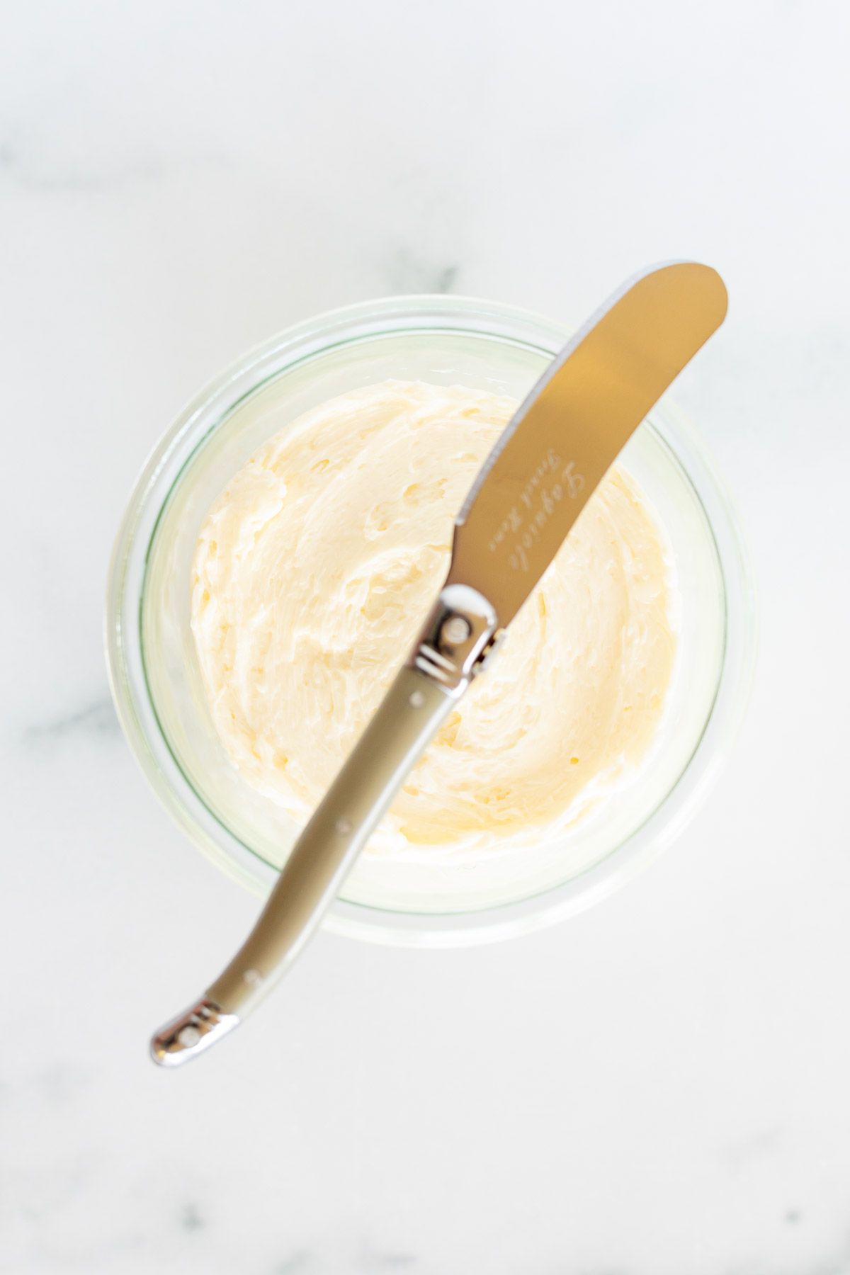 A knife placed over a small glass bowl of homemade butter