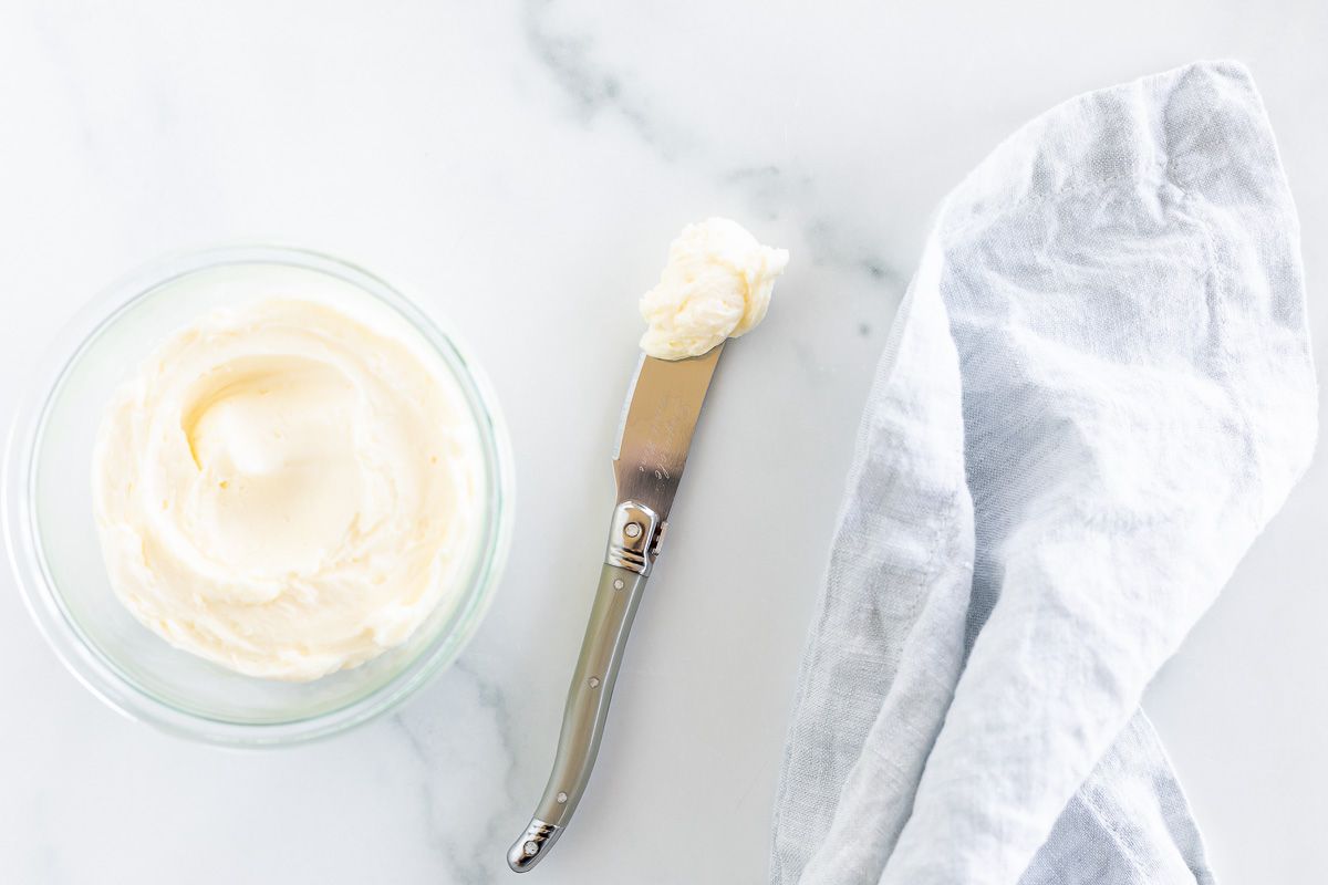 A small glass jar filled with homemade butter, with a knife and blue linen towel to the side