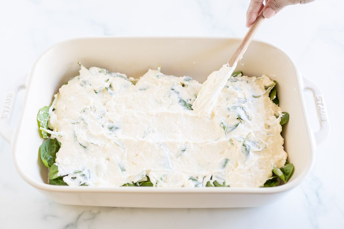 A hand adding cheese on top of a baked chicken and spinach dish.