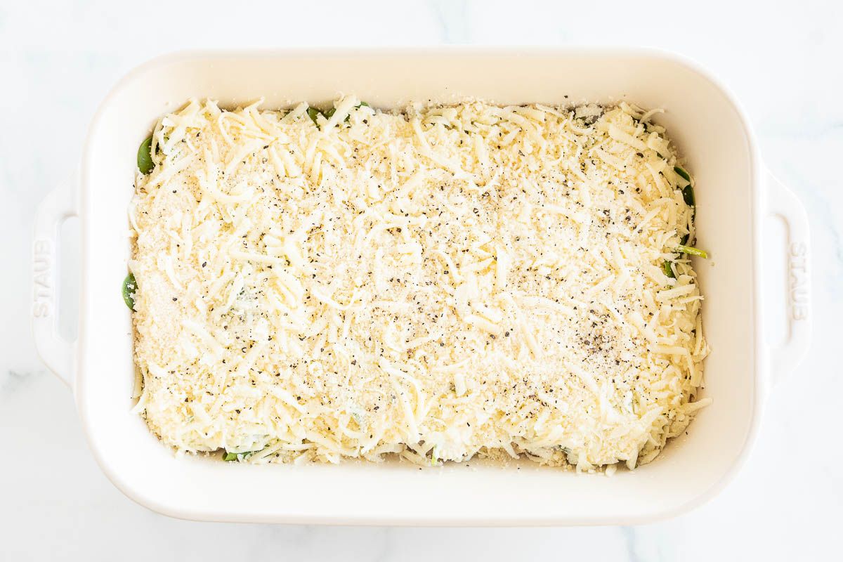 Chicken breasts covered with spinach and cheese in a white casserole dish.