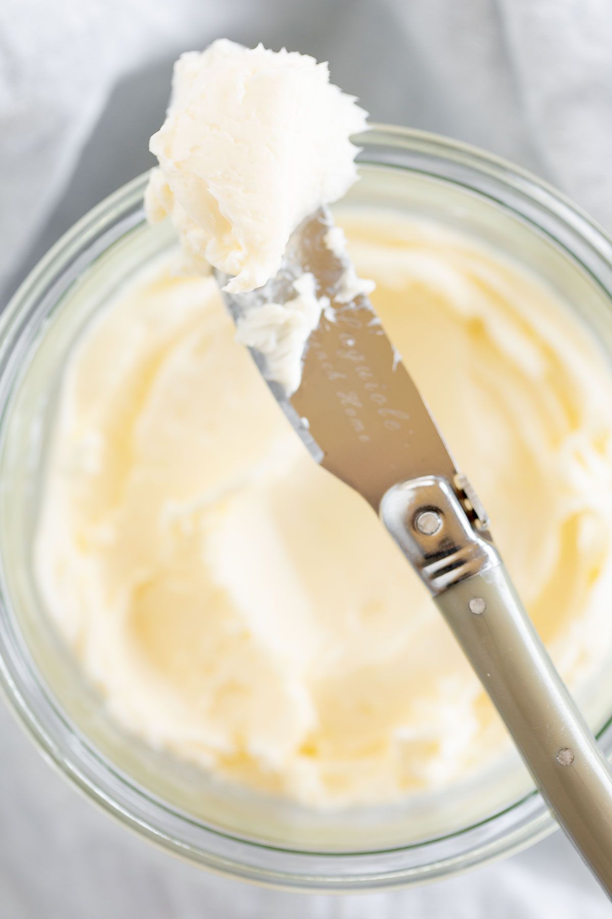 A knife placed over a small glass bowl of homemade butter